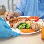 Healthcare worker serving food to an elderly patient.