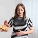 Woman refusing food, with hand on her stomach.
