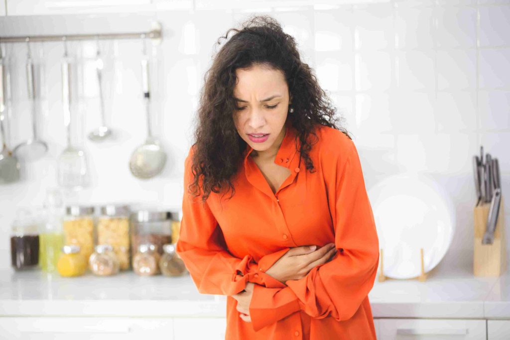 Woman holding her stomach in the kitchen.