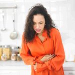Woman holding her stomach in the kitchen.
