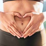 Woman making a heart shape with her hands on her belly.