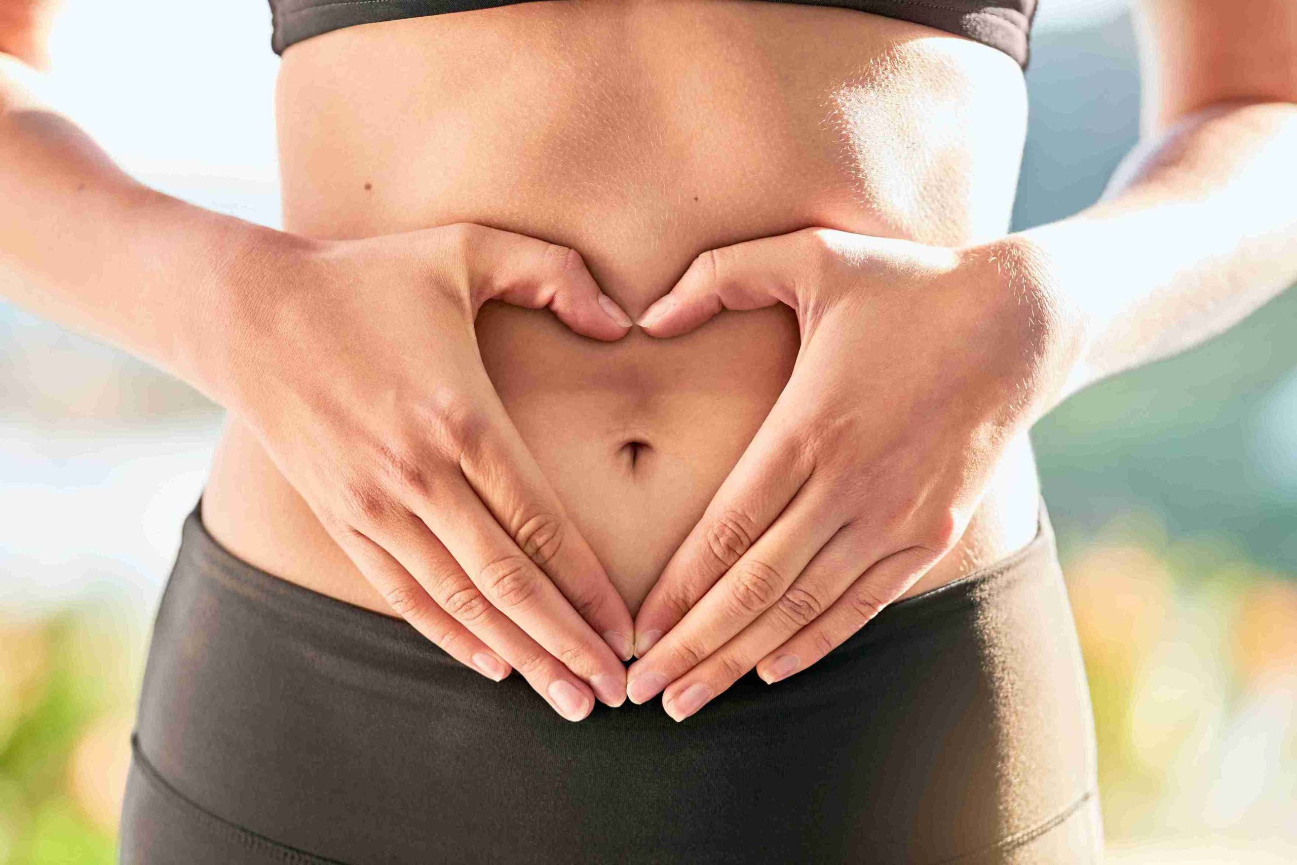 Woman making a heart shape with her hands on her belly.