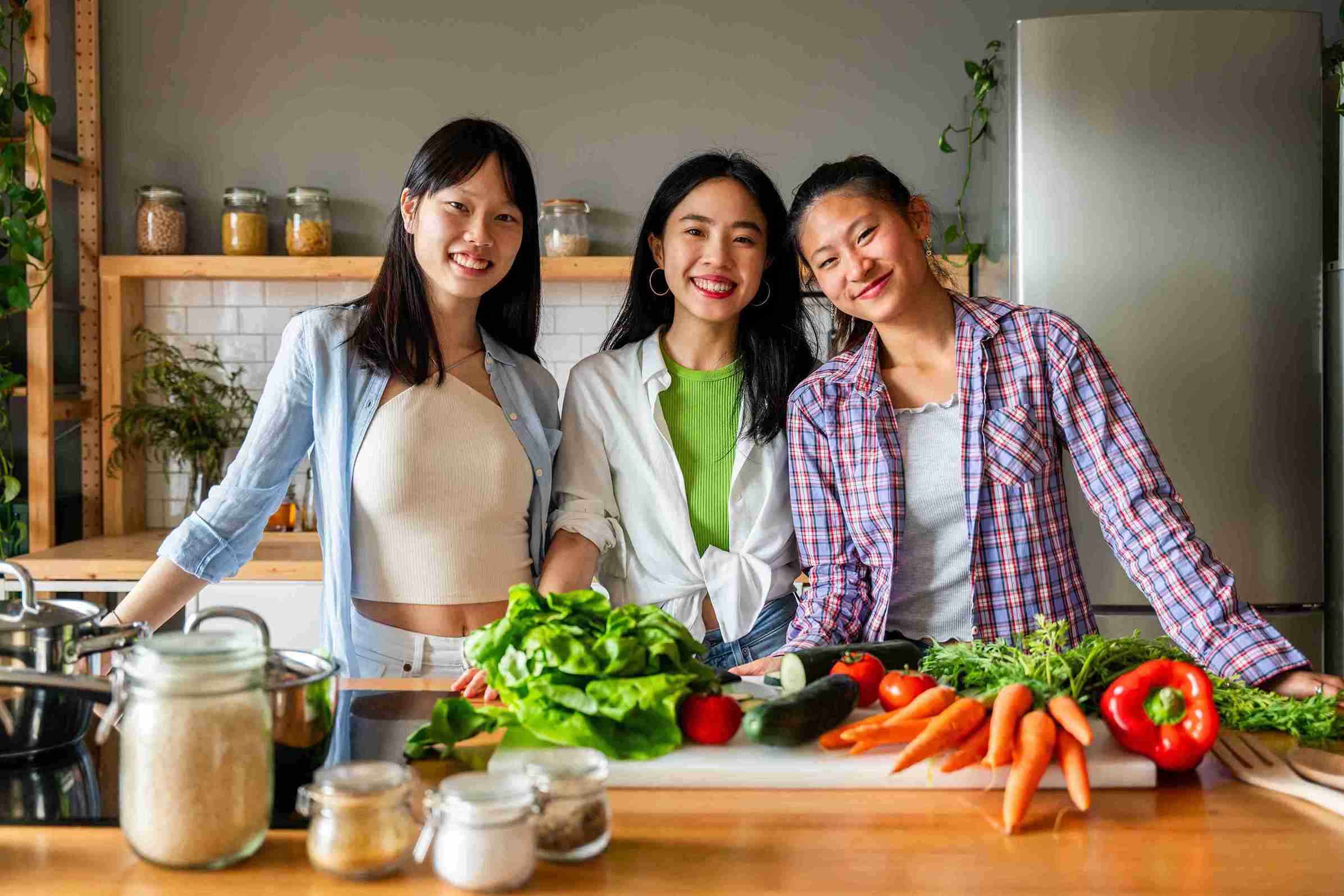 Three young women smiling and preparing fresh vegetables.